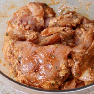 raw chicken thighs covered in marinade in large glass bowl