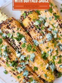 grilled corn on the cob on a plate topped with blue cheese crumbles and fresh cilantro