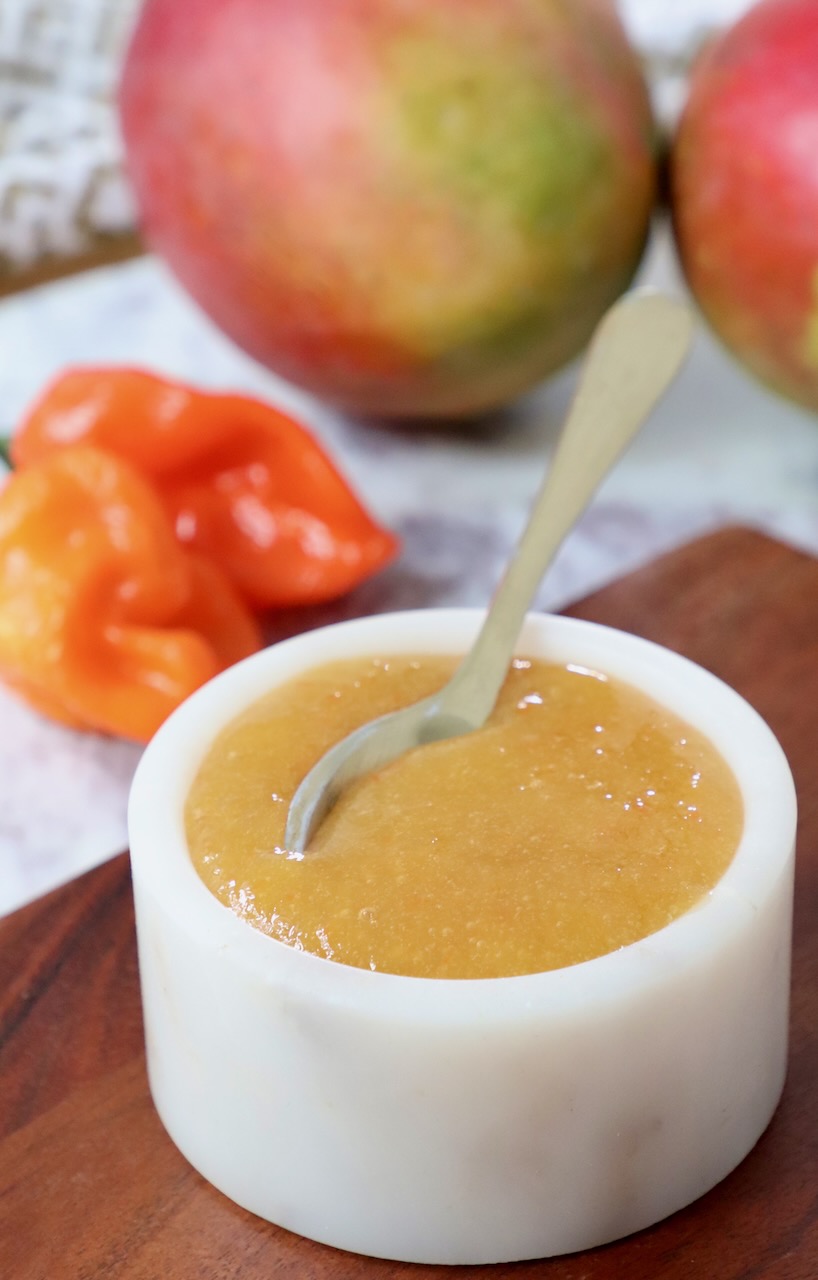 mango habanero sauce in a bowl with a spoon and fresh habaneros and mangos in the background