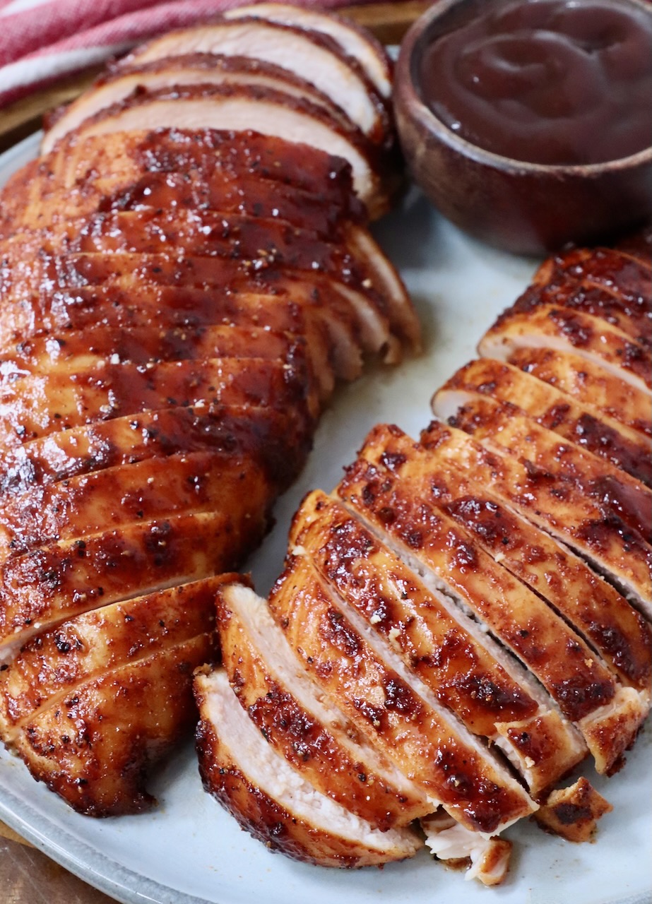 sliced smoked chicken breasts on a plate with a small bowl of bbq sauce