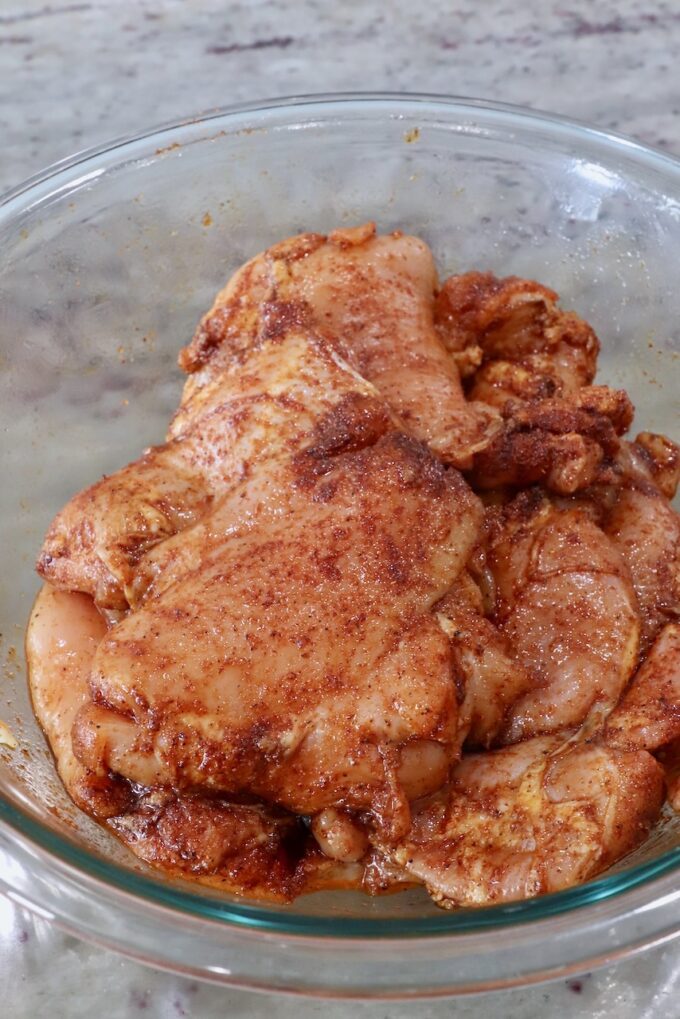 seasoned, raw chicken thighs in a glass bowl
