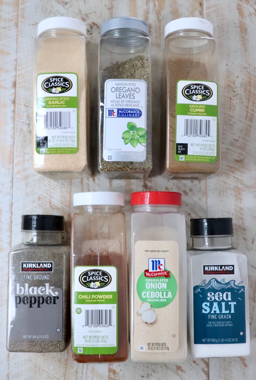 spices in plastic containers lined up on a white wood board