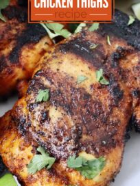 grilled chicken thighs stacked up on a plate with lime wedges on the side