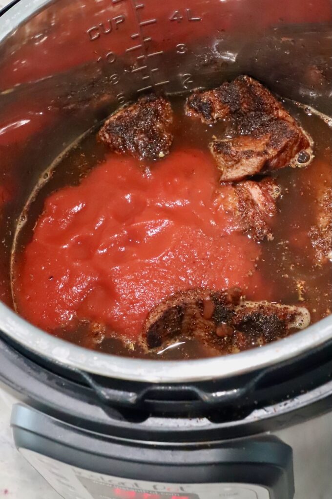 seasoned, seared beef in an Instant Pot with tomato sauce and beef broth