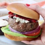 hand holding a lamb burger on a bun over a plate