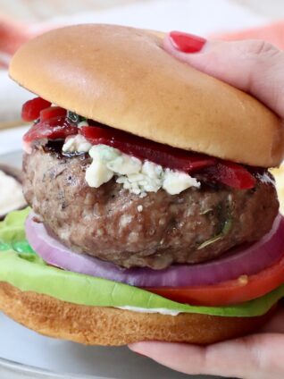 hand holding a lamb burger on a bun over a plate