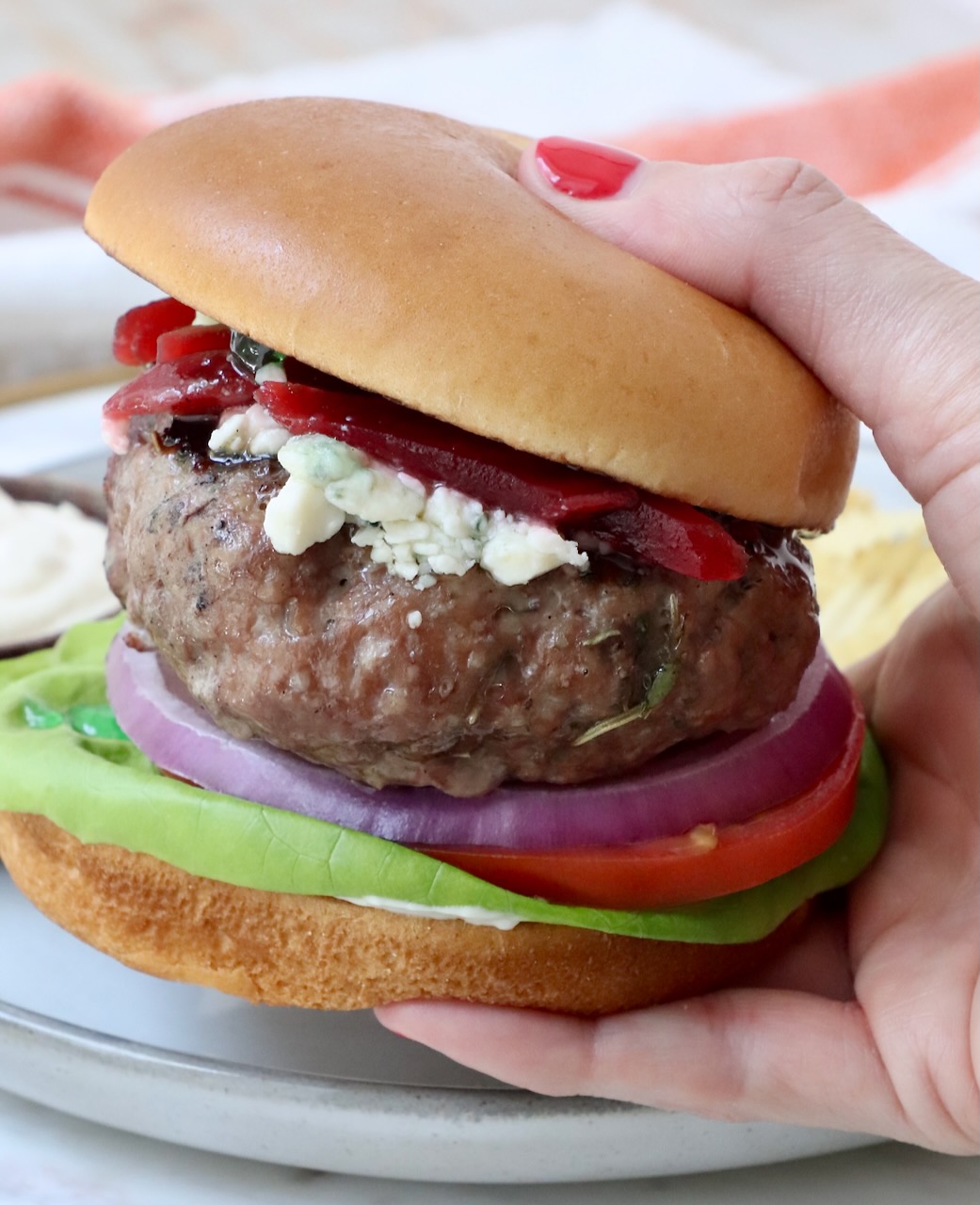 hand holding a lamb burger over a plate