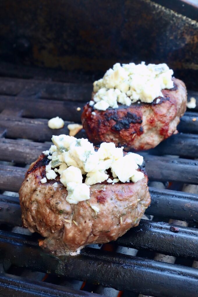 cooked lamb burger patties on a grill topped with blue cheese crumbles
