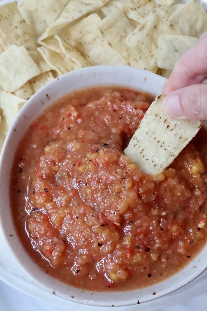 hand dipping a tortilla chip in a bowl of peach salsa
