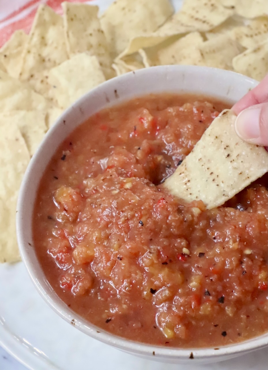 hand dipping a tortilla chip in a bowl of peach salsa
