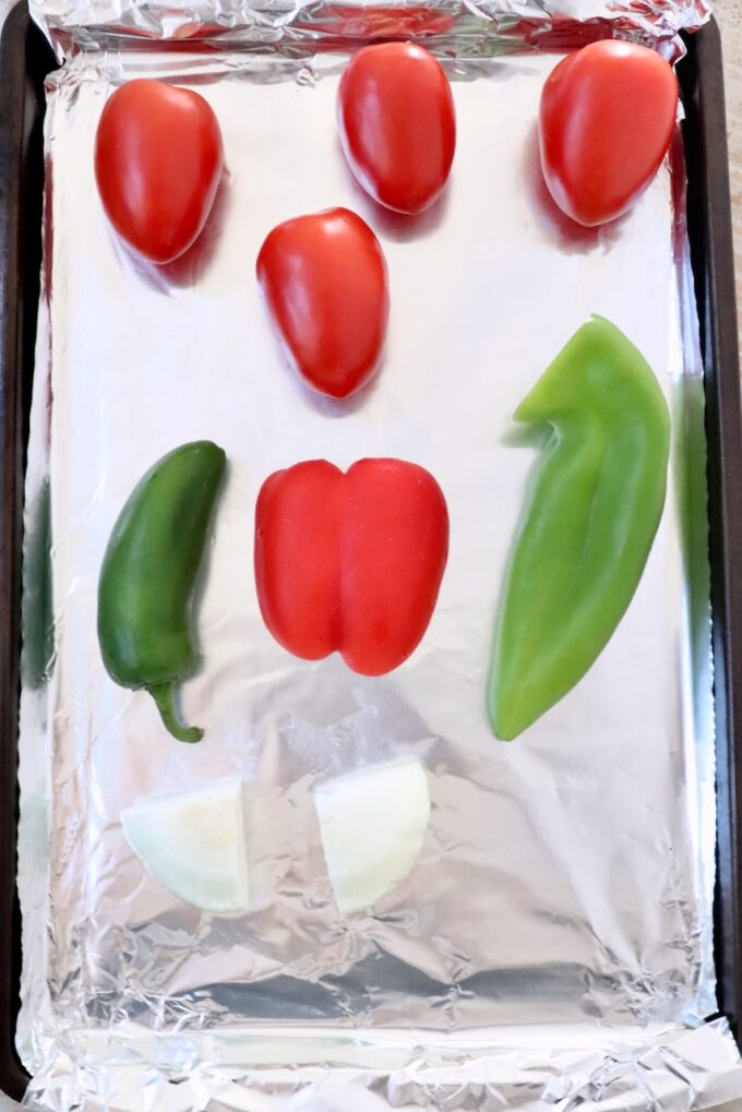 roma tomatoes, peppers and onions on a foil lined baking sheet