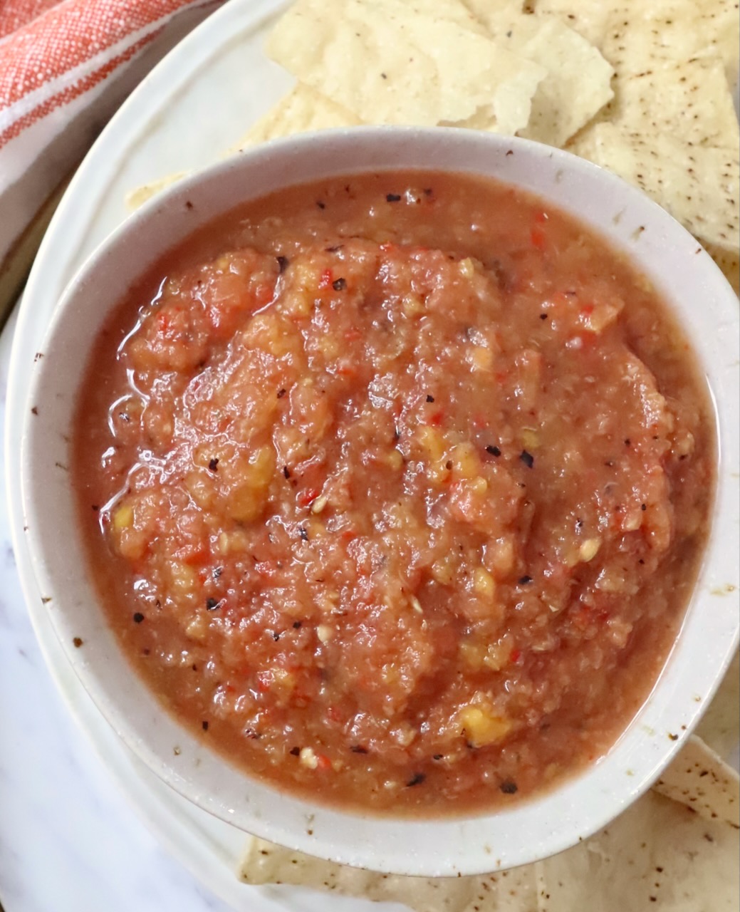 peach salsa in a bowl with tortilla chips surrounding the bowl
