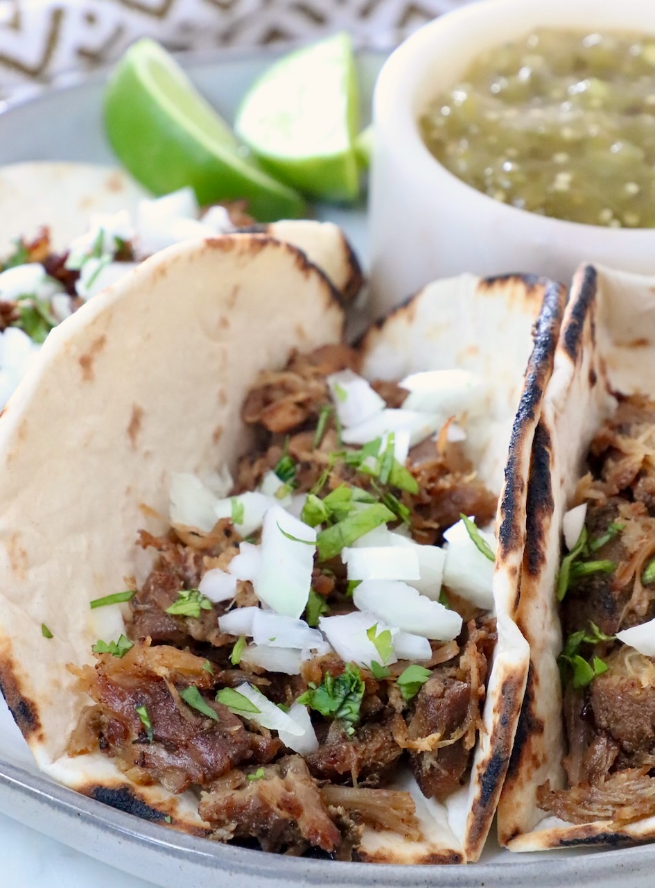 shredded pork in tortillas on plate, topped with diced onions and fresh chopped cilantro