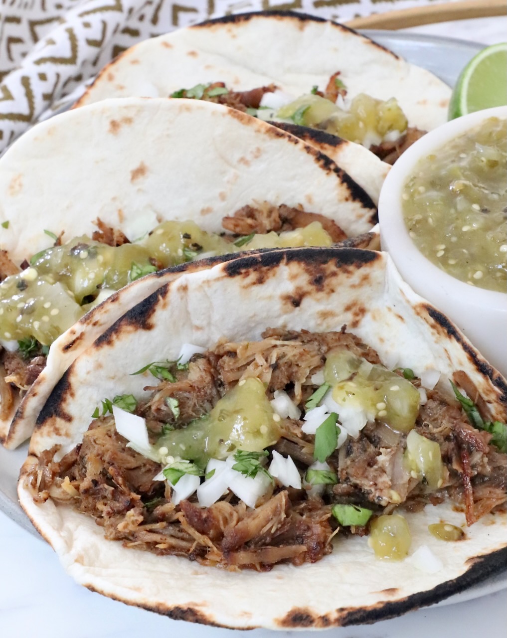 carnitas tacos on a plate with tomatillo salsa on the tacos and in a bowl on the side