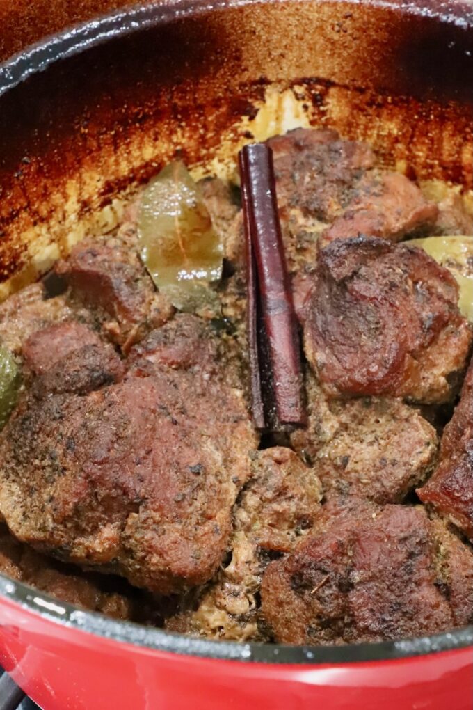 cooked pieces of pork in a large cast iron dutch oven with a cinnamon stick and bay leaves