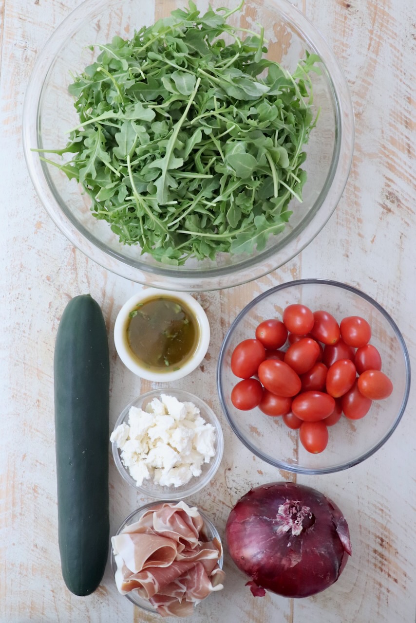 ingredients for cucumber prosciutto salad on a white wood board