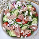 salad in a bowl with prosciutto, sliced cucumbers, feta cheese and tomatoes