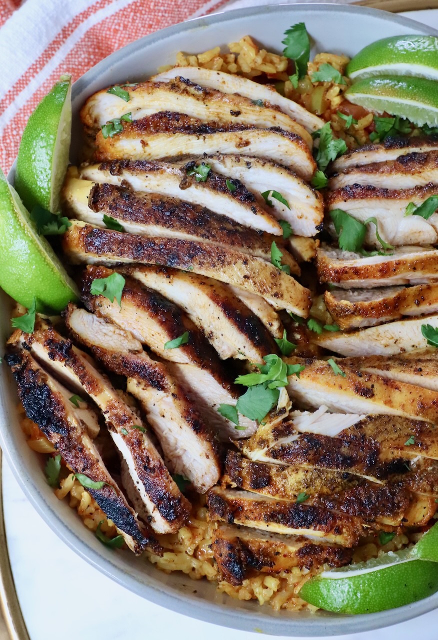 sliced chicken in a bowl with lime wedges on top of yellow rice
