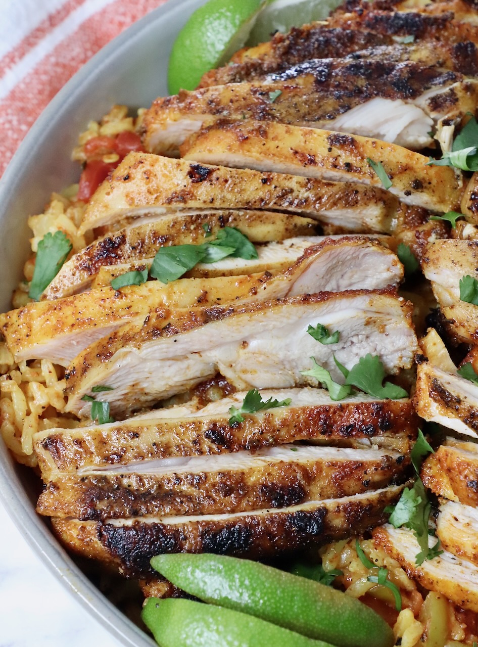 sliced grilled chicken thighs in a bowl with rice and lime wedges