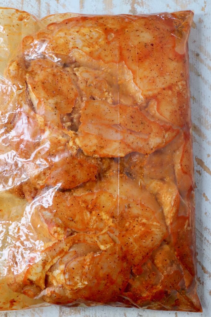 chicken thighs marinating in sazon seasoning in a large plastic bag