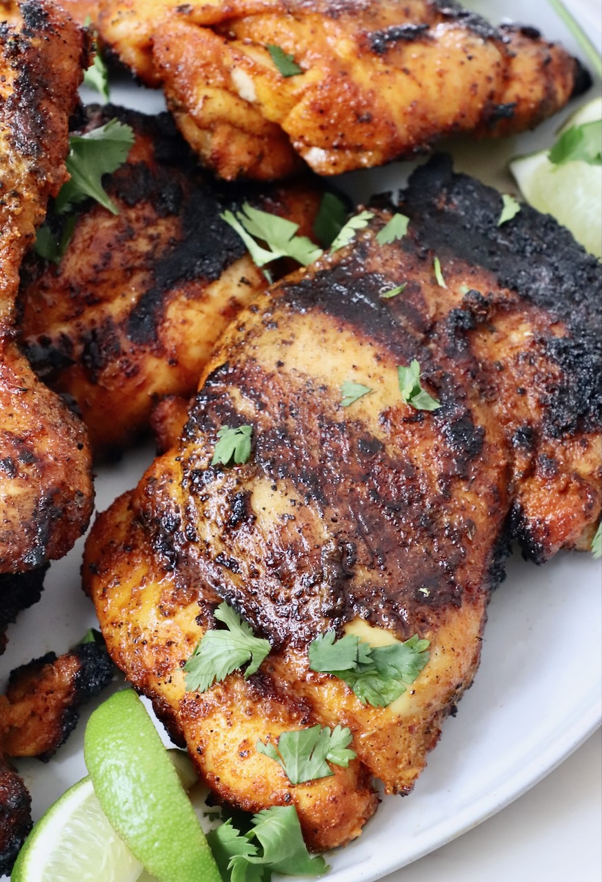 grilled chicken thighs stacked up on a plate with lime wedges on the side