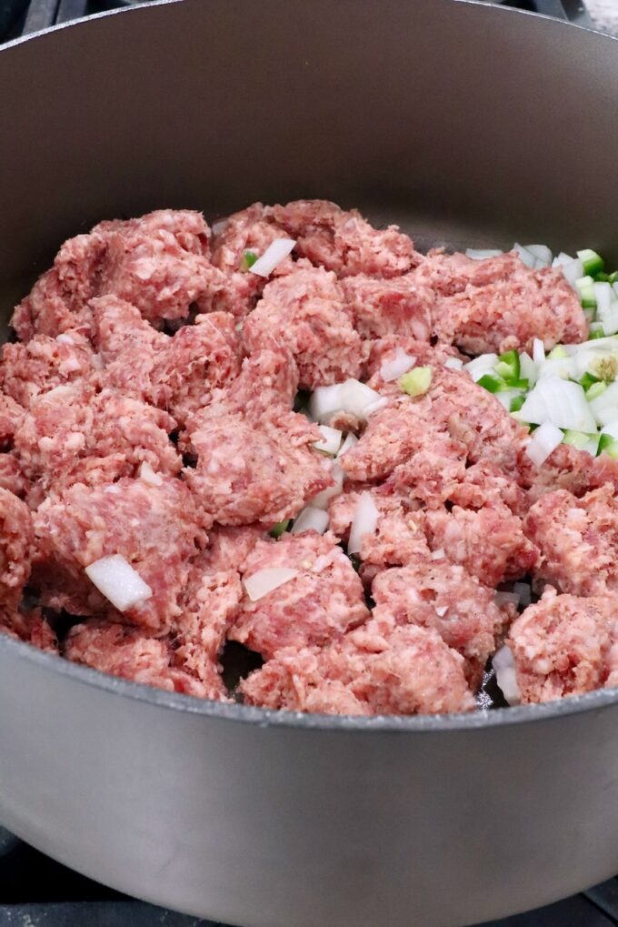 uncooked sausage in a large pot with diced onions and jalapenos