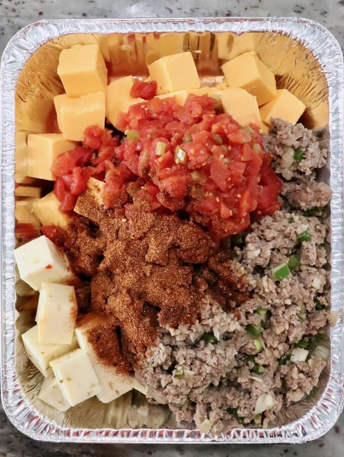 cubes of cheese, cooked, crumbled sausage, diced tomatoes and chili seasoning in an aluminum pan
