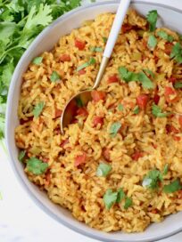 yellow rice in a bowl with a spoon topped with fresh cilantro leaves