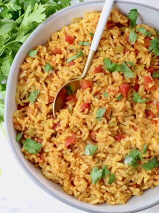 yellow rice in a bowl with a spoon topped with fresh cilantro leaves