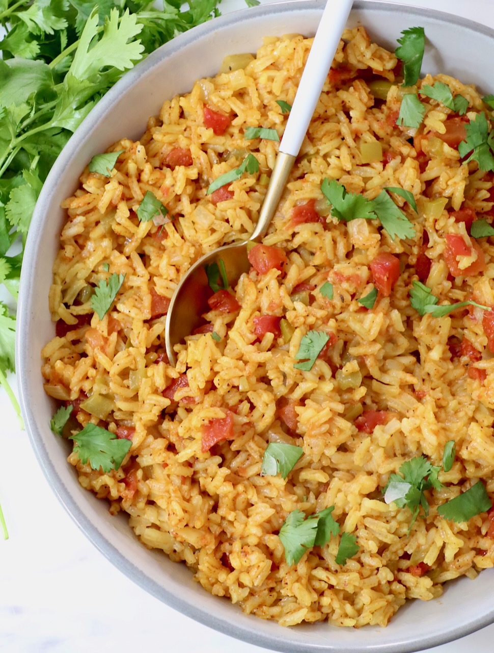 yellow rice in a bowl with a spoon topped with fresh cilantro leaves