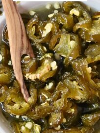 sliced candied jalapenos in a bowl with a wooden fork