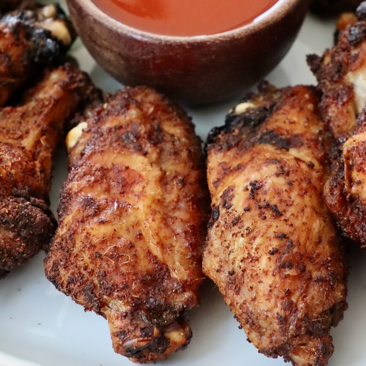 baked chicken wings on a plate with a small bowl of buffalo sauce