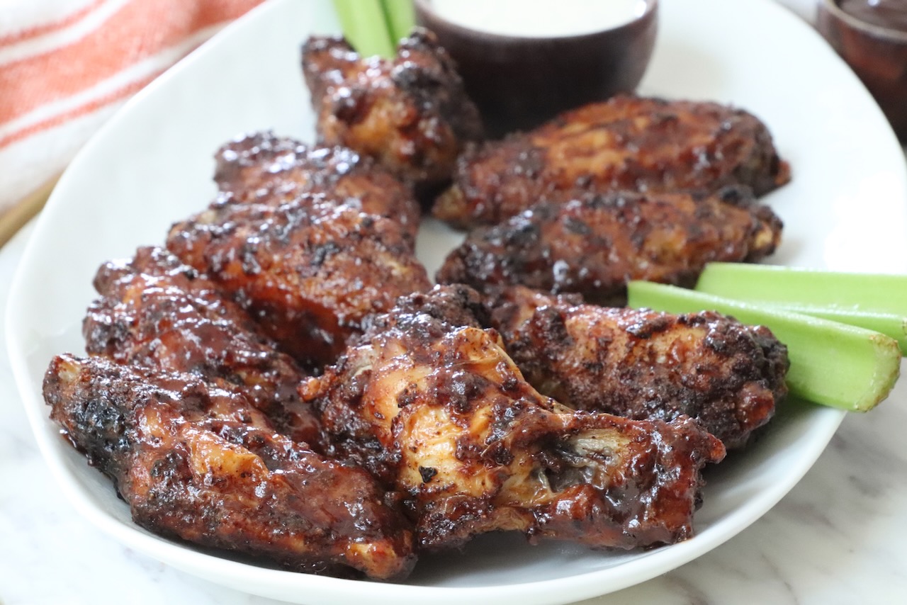 cooked chicken wings tossed in bbq sauce on a plate with celery sticks