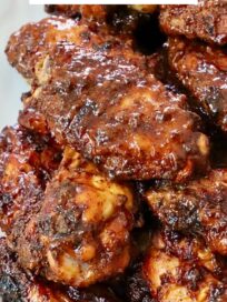 cooked chicken wings tossed in bbq sauce stacked up on a plate