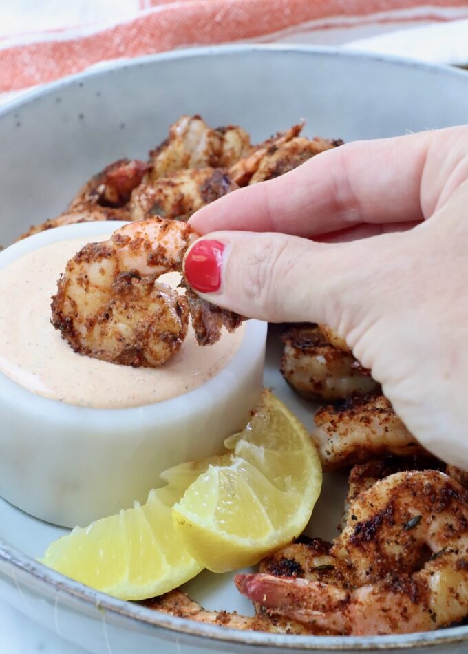 hand dipping a cooked shrimp into a bowl of creamy sauce
