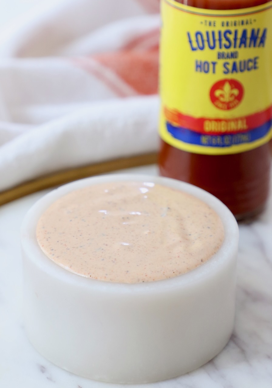 creamy cajun sauce in a small white bowl with a bottle of hot sauce behind it