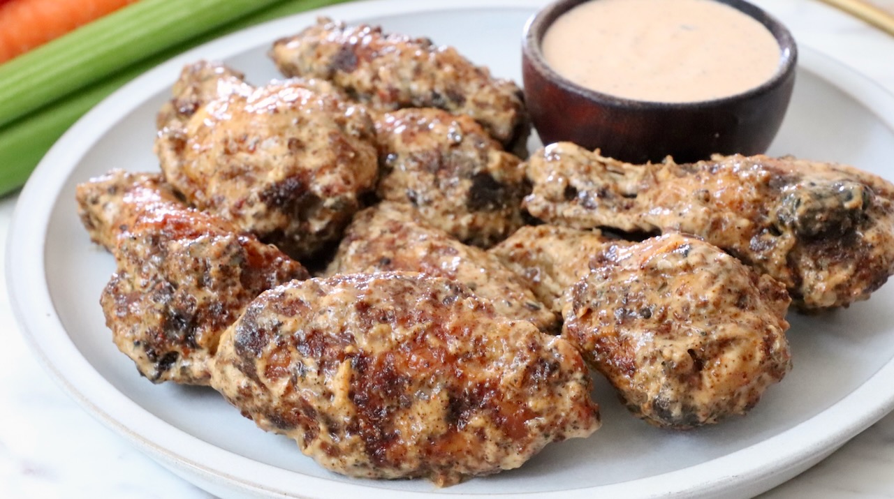 cooked chicken wings tossed in sauce on a plate with a small bowl of creamy sauce