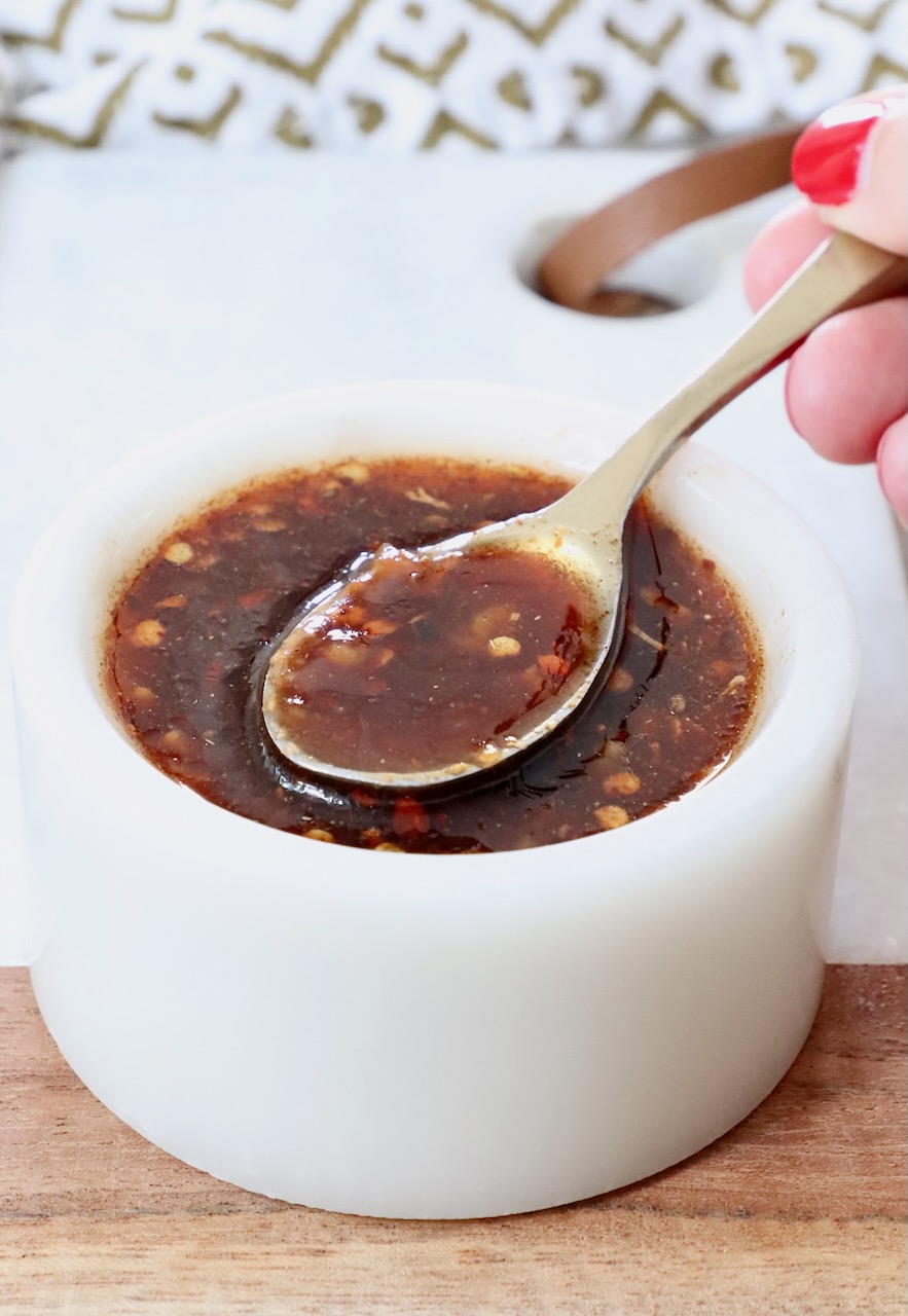 hand holding a spoon dipped into a bowl of sauce