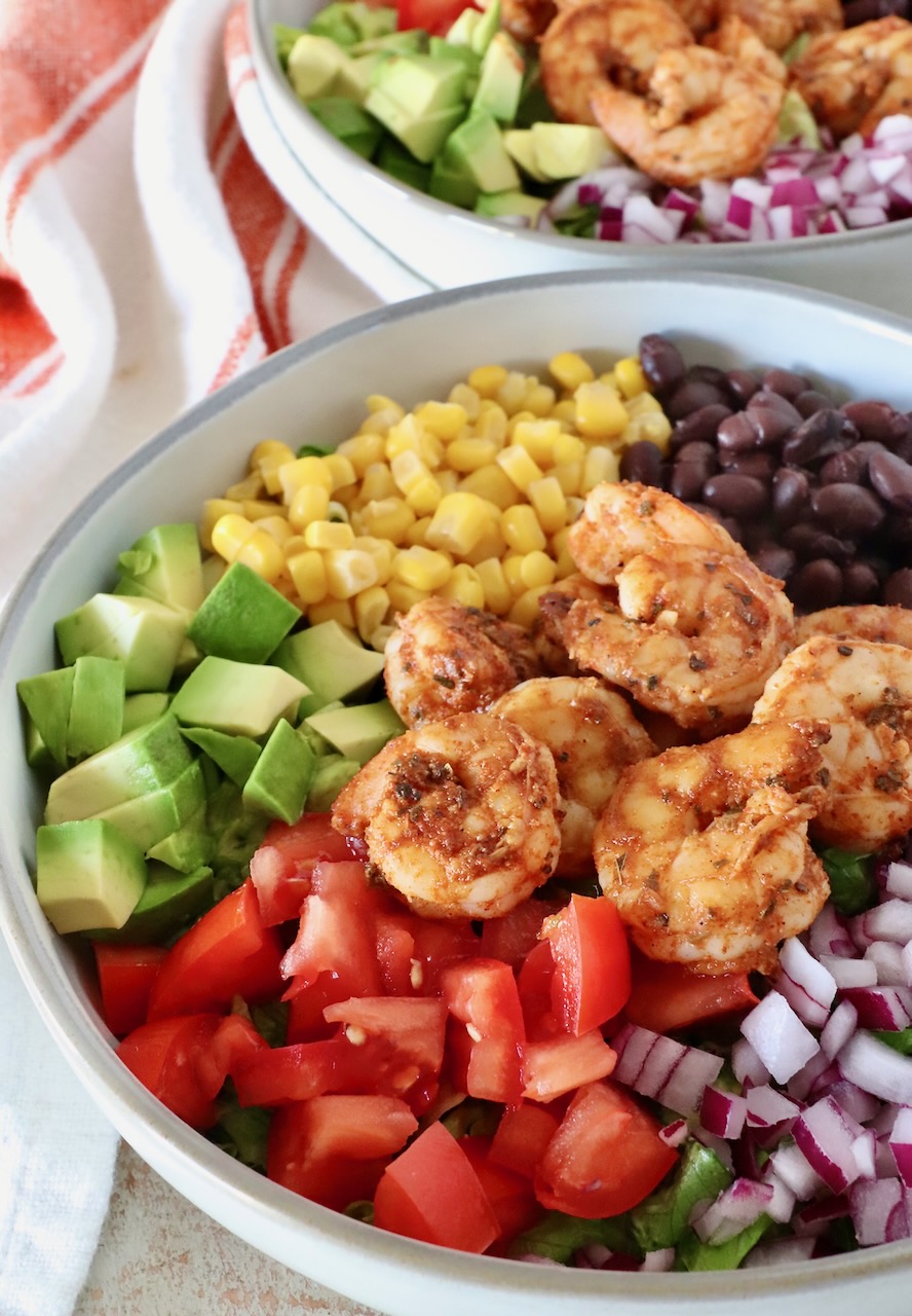 salad in a bowl with seasoned shrimp, diced avocado, red onions, black beans, corn, and tomatoes