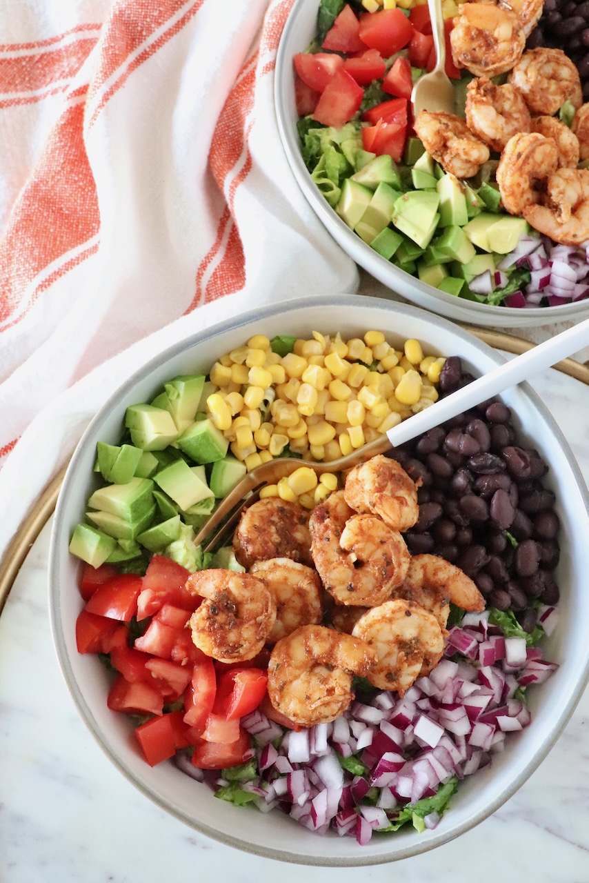 salad topped with shrimp, onion, tomato, beans, corn and avocado in a bowl with a fork