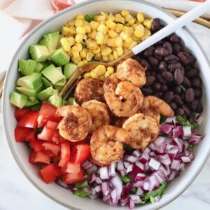 salad topped with shrimp, onion, tomato, beans, corn and avocado in a bowl with a fork