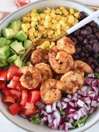 salad topped with shrimp, onion, tomato, beans, corn and avocado in a bowl with a fork