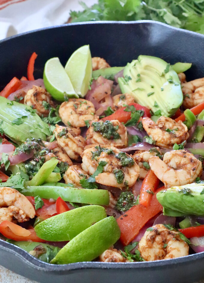 shrimp fajitas in a cast iron skillet covered with cilantro chimichurri sauce and sliced avocado