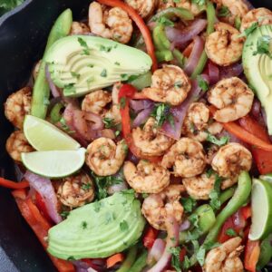 shrimp fajitas in a cast iron skillet topped with sliced avocado and lime wedges