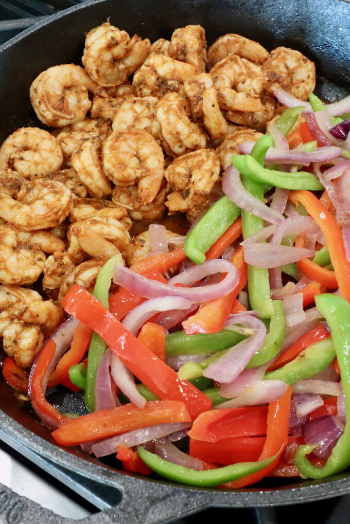 seasoned cooked shrimp in a cast iron skillet with sliced bell peppers and onions