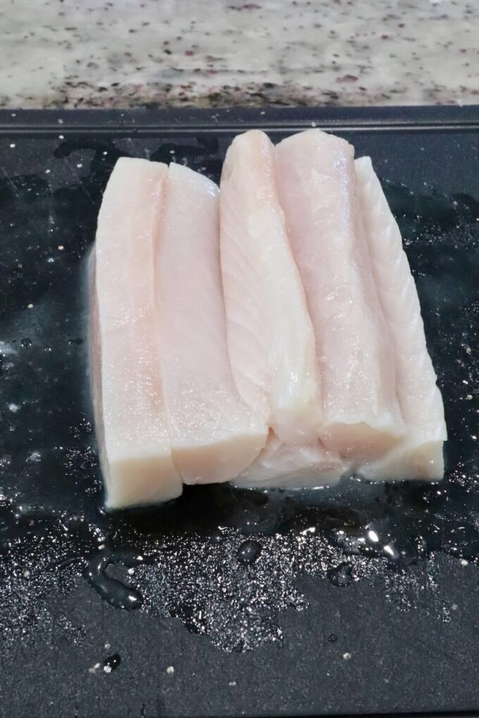raw mahi mahi fish fillets cut into strips on a black cutting board.
