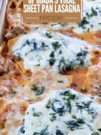 Close-up of a golden sheet pan lasagna topped with melted cheese and herbs. Text overlay reads "The Fall Version of Giada's Viral Sheet Pan Lasagna Recipe."