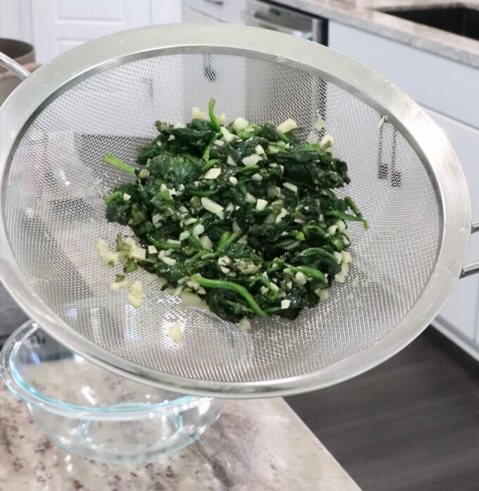 cooked spinach and garlic in a mesh strainer