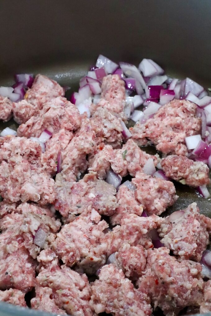 raw crumbled sausage in a pan with diced onions