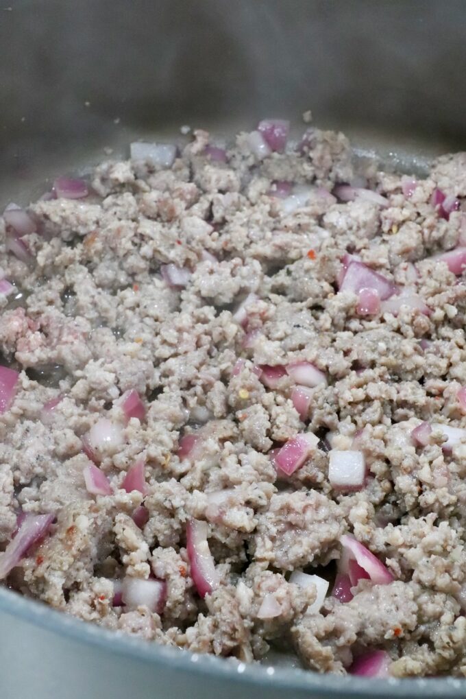 cooked, crumbled sausage in a pan with diced onions
